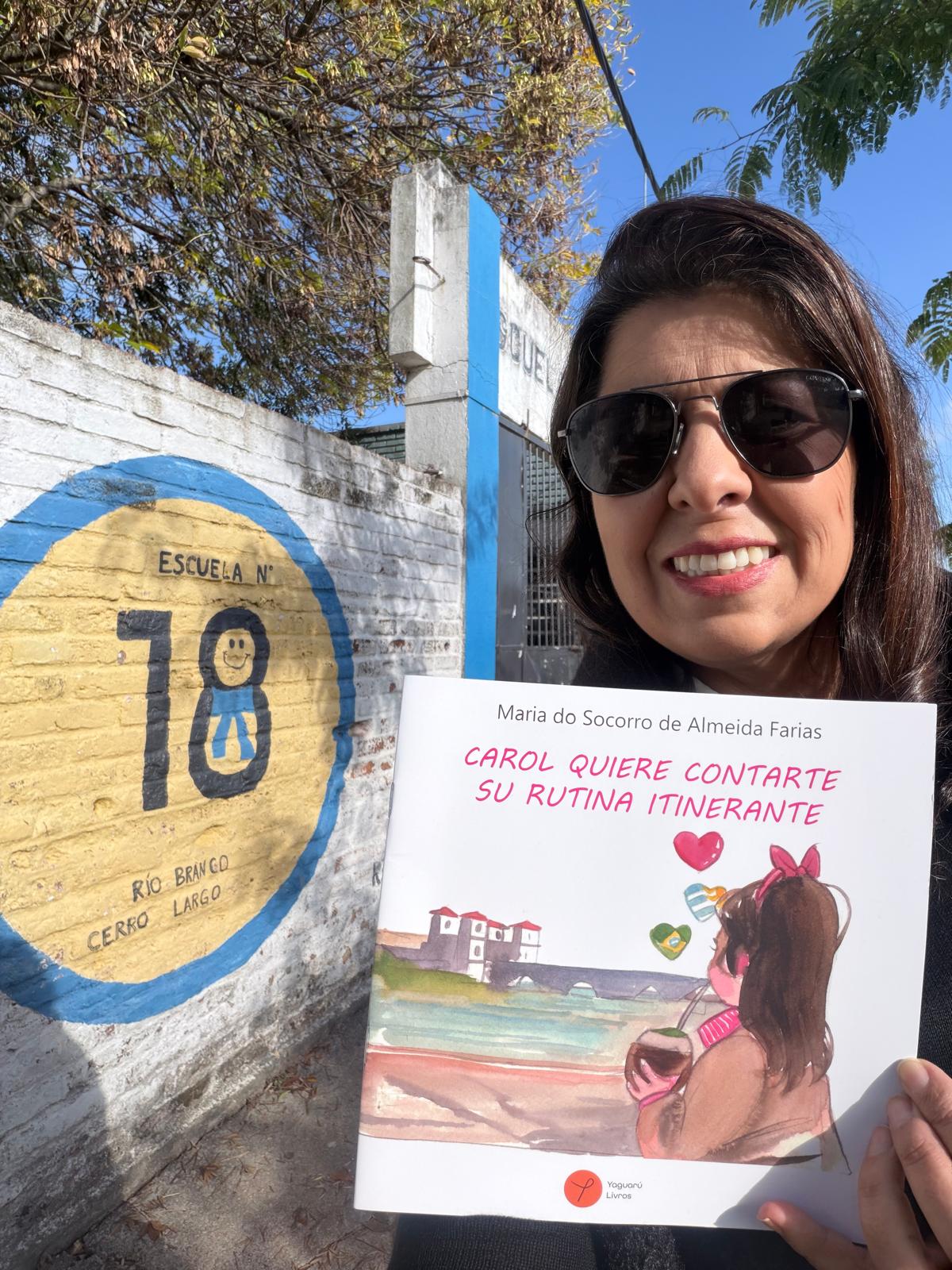 Maria do Socorro com o livro Carol em frente à Escuela 18 em Río Branco, Uruguay
